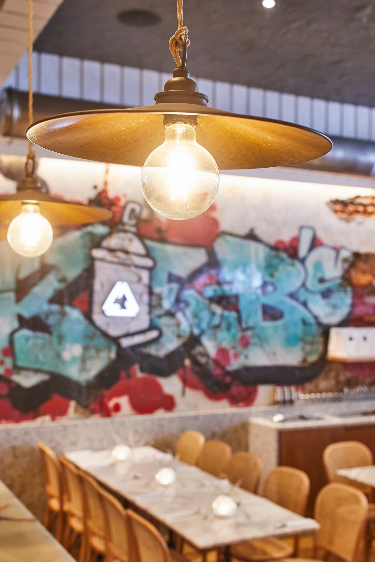 A section of Frankie B's Food House Parramatta featuring a long dining table, graffiti wall art, and hanging industrial lights